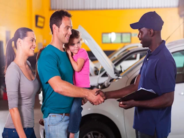 friendly auto mechanic handshaking with family inside repair shop